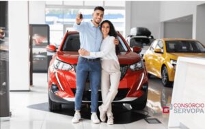 um casal, sentando no capô do carro vermelho, olhando para camera e sorrindo felizes porque foram sorteados no consórcio servopa